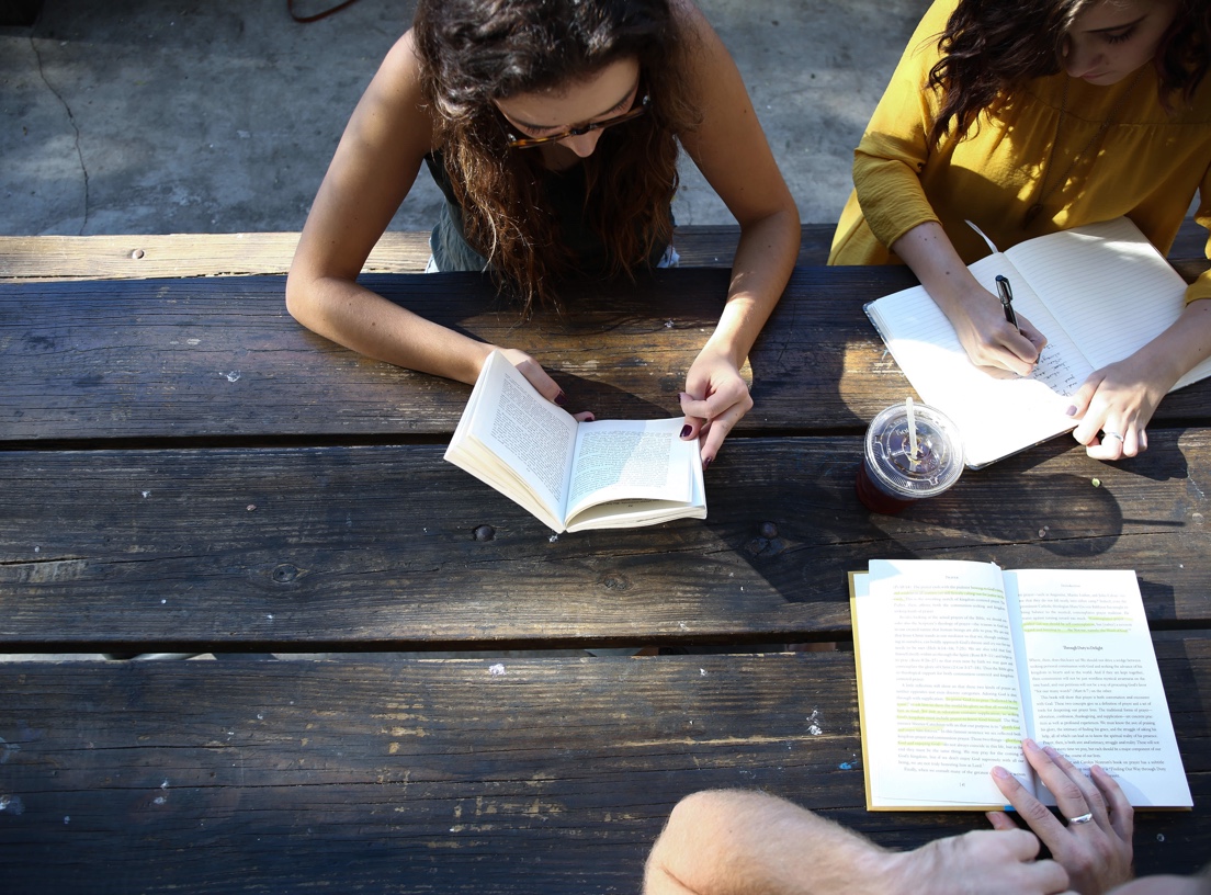 Top down view of three students reading books or taking writen notes at a wooden picnic table