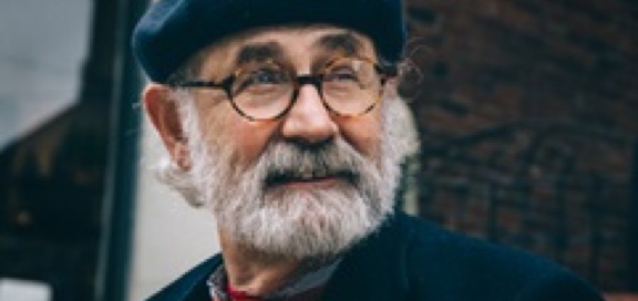 Older man with round glasses, a blue hat and a neatly trimmed salt and pepper beard