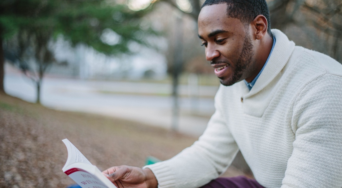 Man in a white sweater reading a book outside